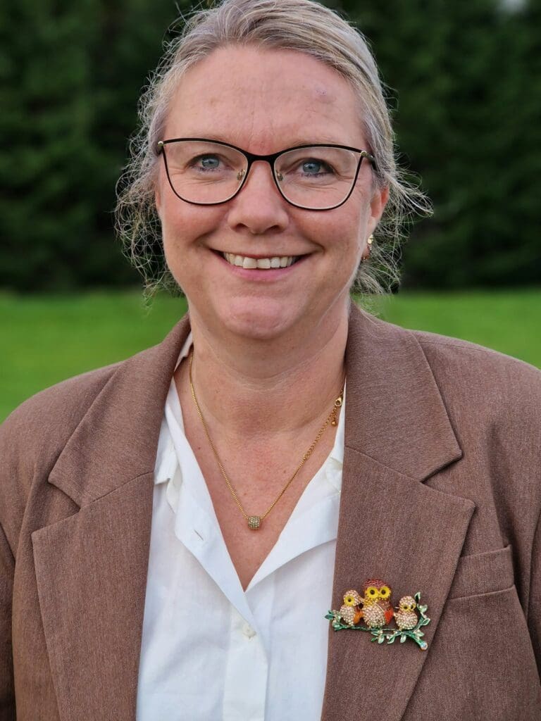 kvinne med brun jakke og lys skjorte, grålig i håret