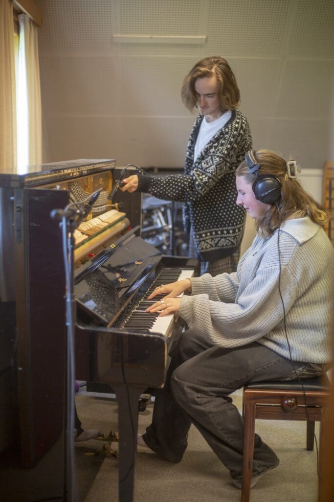 piano og gitar og to elever som spiller i lydstudio