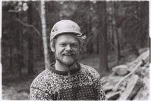 Smilende person i klatrehjelm og mønstret ullgenser i skog, sorthvitt utendørsportrett.